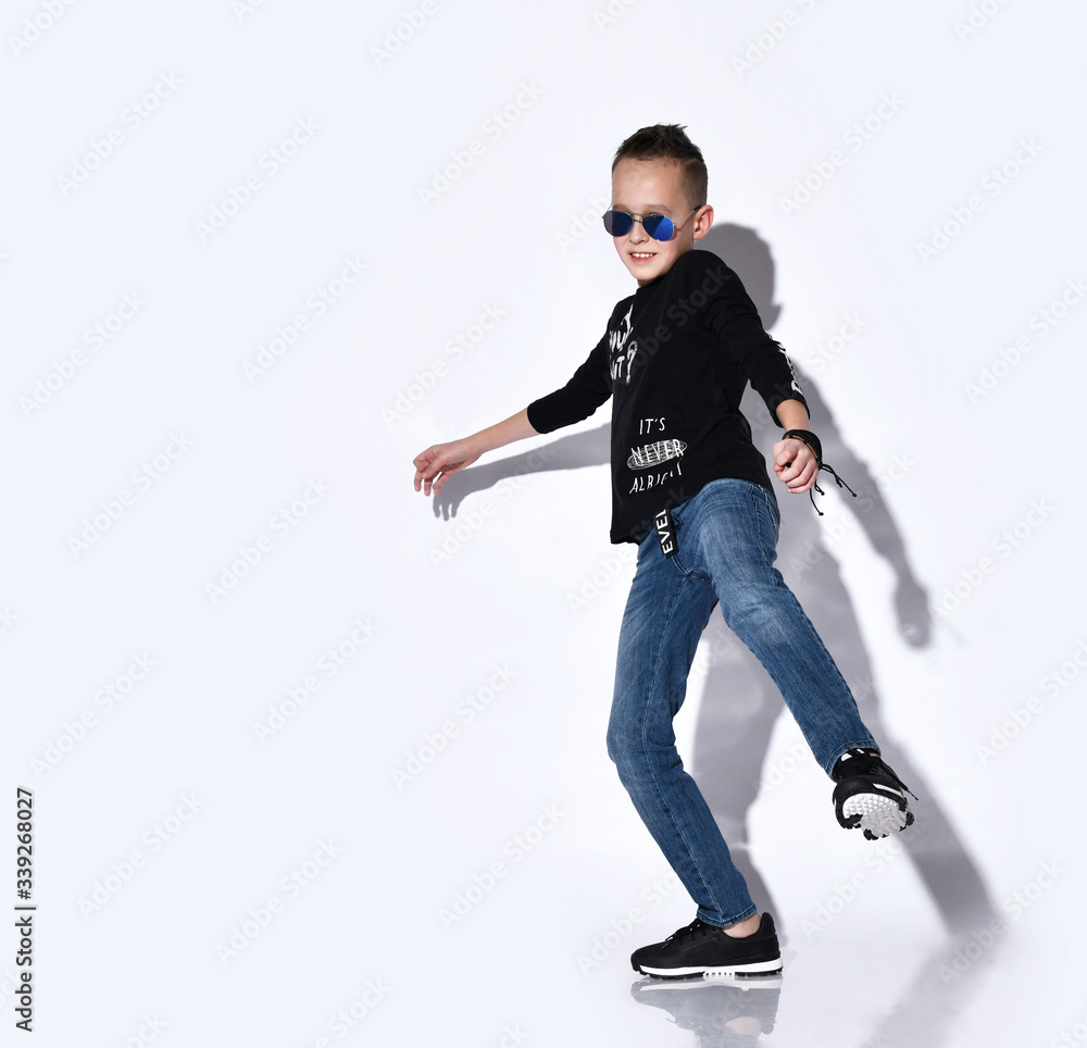 Teenage child in sunglasses, black jumper and sneakers, blue jeans, bracelet. Dancing, posing isolated on white studio background Teenage child in sunglasses, black jumper and sneakers, blue jeans, bracelet. Dancing, posing isolated on white studio background