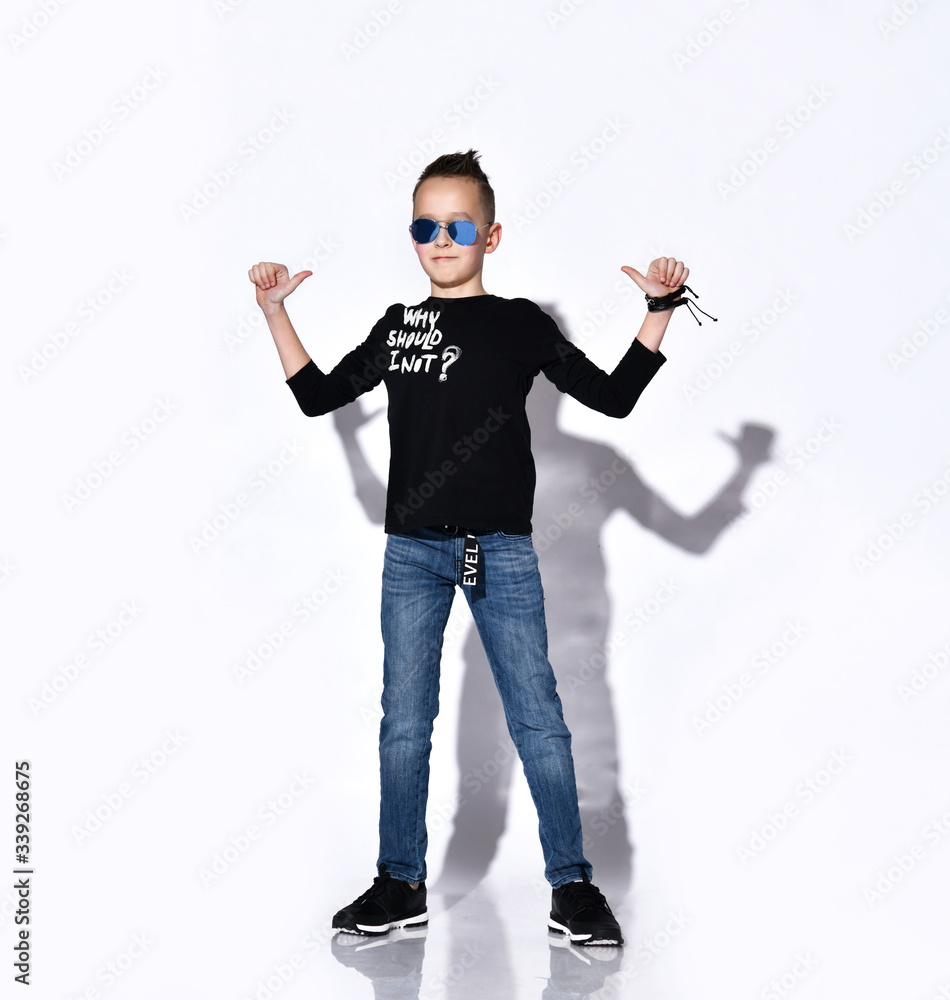 Teenage male in sunglasses, black jumper and sneakers, jeans, bracelet. He smiling, showing thumbs up, posing isolated on white Teenage male in sunglasses, black jumper and sneakers, jeans, bracelet. He smiling, showing thumbs up, posing isolated on white