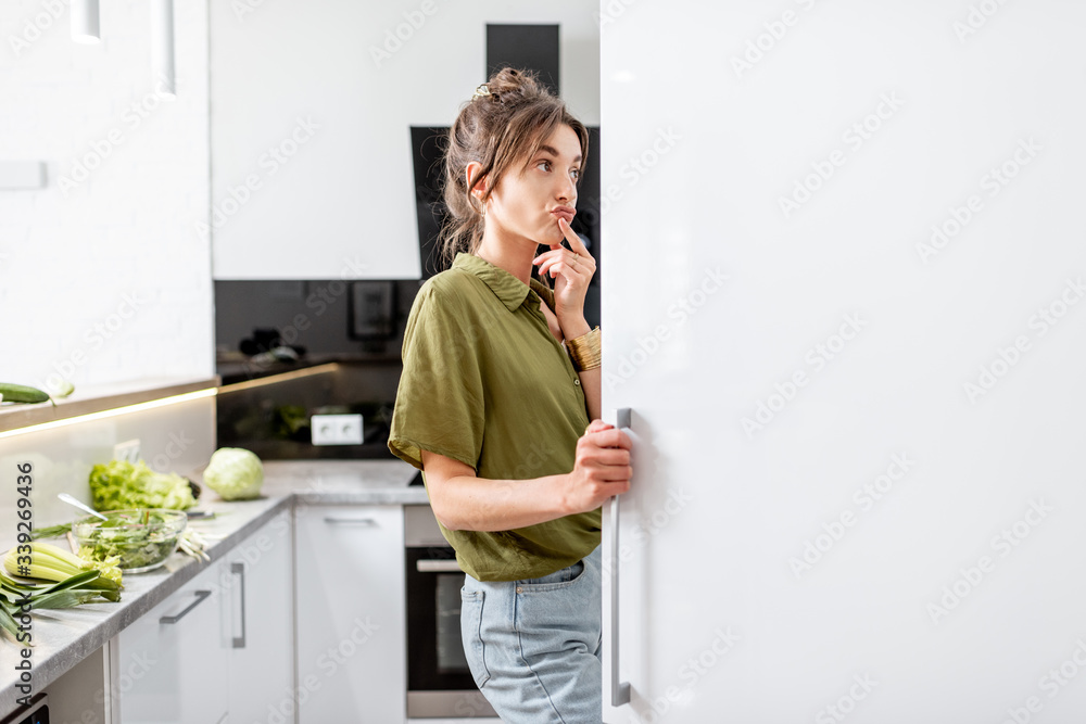 Woman looking into the fridge while cooking healthy food on the modern kitchen at home - obrazy, fototapety, plakaty 