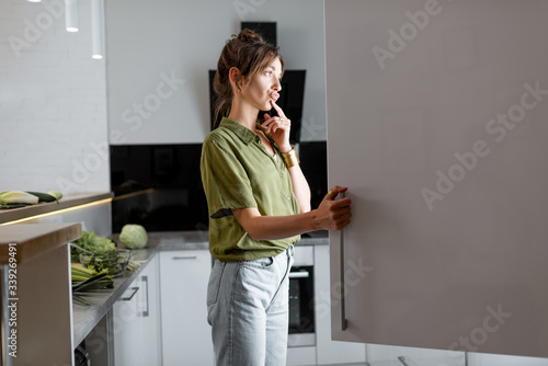 Fototapeta Young woman looking into the fridge, feeling hungry at night