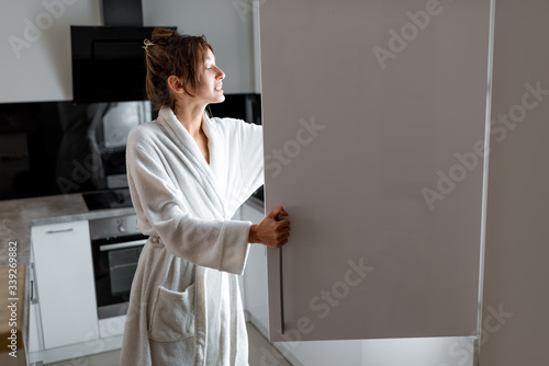 Young woman in bathrobe getting some food from the fridge, feeling hungry at night. Concept of not regular eating and overeating at night