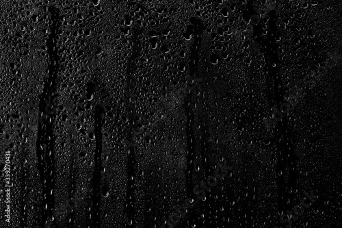 Drops of water flow down the surface of the clear glass on a black background.	 photo