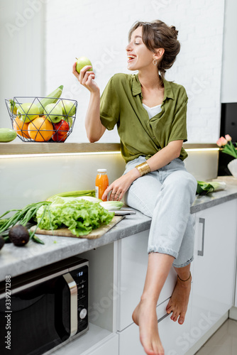 Full length portrait of a young and cheerful woman with healthy raw food on the kitchen at home. Vegetarianism, wellbeing and healthy lifestyle concept