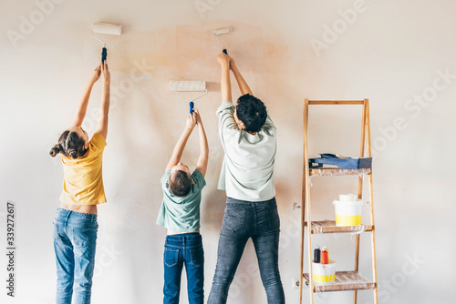 Happy mother, douther and son painting wall with roller. Mom teachs her children painting with roller at home. photo