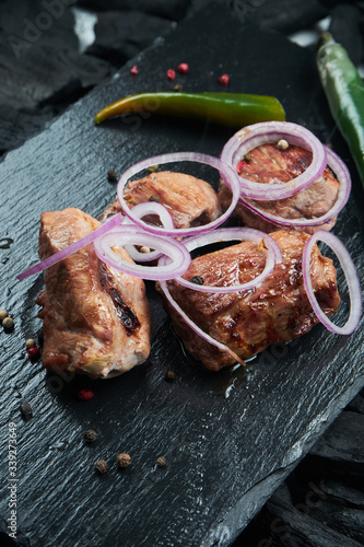 Appetizing beef kebab with spices and onions on a black slate tray on a background of charcoal. Shahlik. Close up portion of grilled meat photo