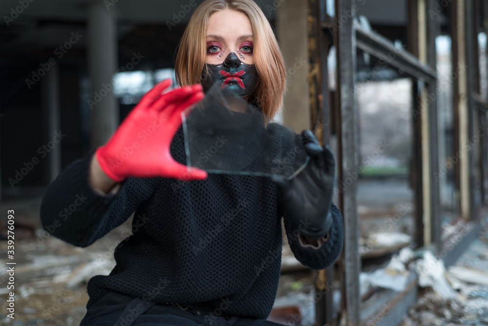 Fototapeta premium beauty portrait of a beautiful girl in a black mask with rhinestones, cool designer makeup. The girl is crying emotionally, holding a broken glass in her hand.