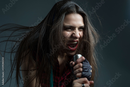 Sexy young girl aggressively sings hard rock and roll music. Emotionally holds two fingers up. Studio photo on a gray background.