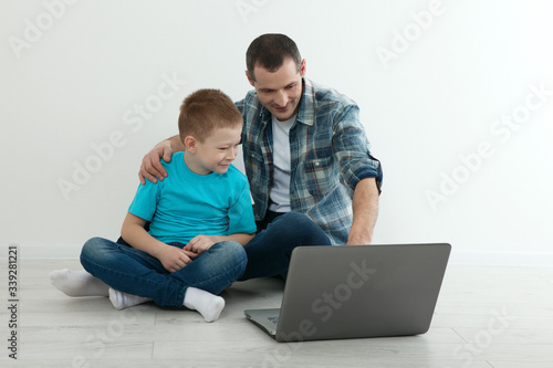 Father and son using laptop sitting on the hardwood floor together at home