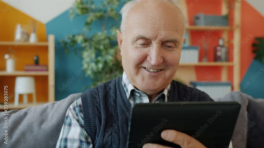 Elderly man touching tablet screen relaxing on couch in apartment using gadget alone enjoying internet content. Lifestyle, devices and retirement concept. Elderly man touching tablet screen relaxing on couch in apartment using gadget alone enjoying internet content. Lifestyle, devices and retirement concept.