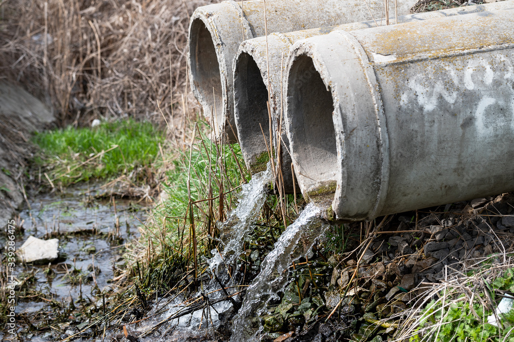 Three old concrete sewer pipes with flowing water. city drainage system. sewer sewage pollute the environment Three old concrete sewer pipes with flowing water. city drainage system. sewer sewage pollute the environment