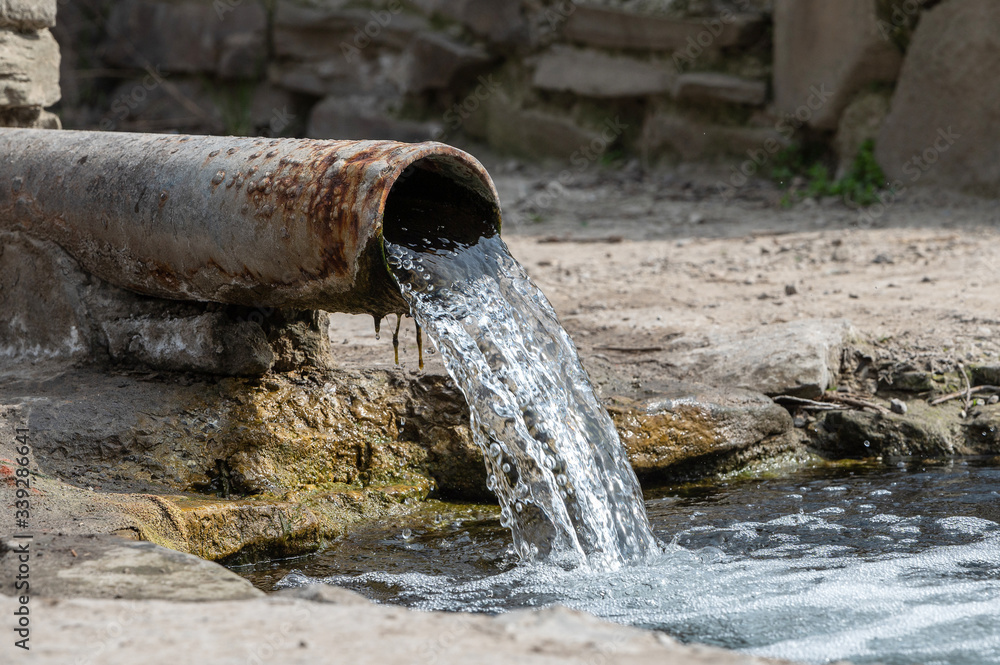 rusty pipe with flowing water into the river. spring with clear spring water. drainage system or sewage system