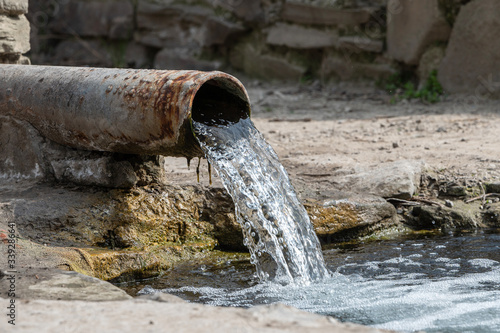 Obraz na płótnie rusty pipe with flowing water into the river. spring with clear spring water. drainage system or sewage system w salonie