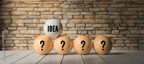 wooden balls with questionmarks and one with the word IDEA in front of a brick wall background