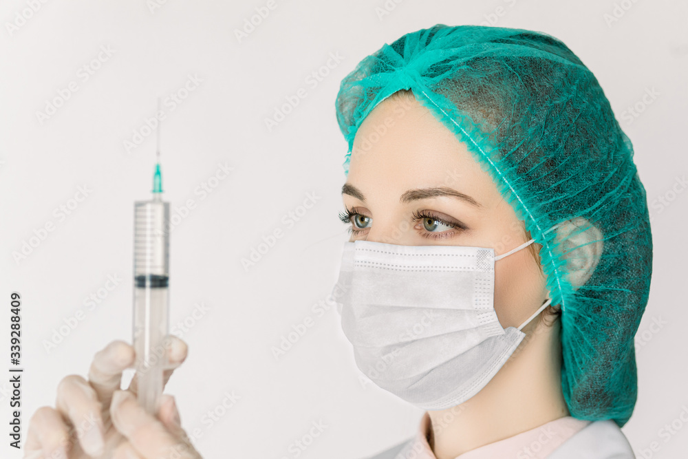 Young woman nurse or doctor in white lab coat, cap and mask, with syringe in hands, prepares syringe for vaccination, isolated on white background. Medical and health care concept Young woman nurse or doctor in white lab coat, cap and mask, with syringe in hands, prepares syringe for vaccination, isolated on white background. Medical and health care concept