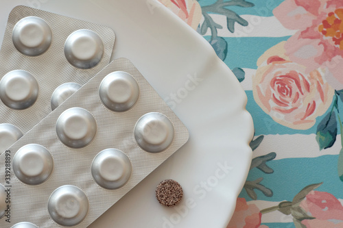 Iron pills on a plate. Many tablets of Ferrous sulfate. Supplement use for Iron Deficiency Anemia. Floral retro background. Pastel color.
