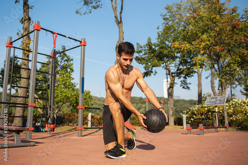 Fit guy doing exercises using a ball outdoors. Young athletic man training in city park