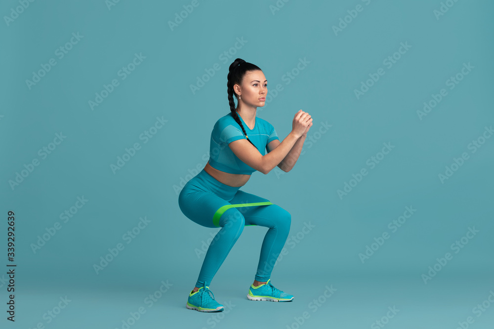 Lower body. Beautiful young female athlete practicing in studio, monochrome blue portrait. Sportive fit brunette model with elastics. Body building, healthy lifestyle, beauty and action concept.