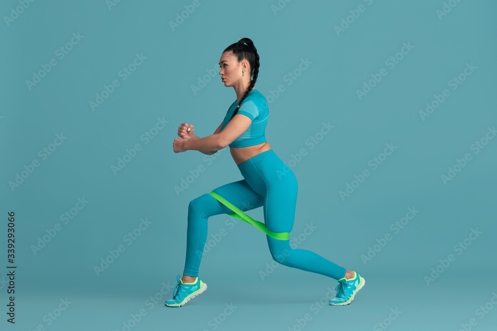 Lower body. Beautiful young female athlete practicing in studio, monochrome blue portrait. Sportive fit brunette model with elastics. Body building, healthy lifestyle, beauty and action concept. Lower body. Beautiful young female athlete practicing in studio, monochrome blue portrait. Sportive fit brunette model with elastics. Body building, healthy lifestyle, beauty and action concept.