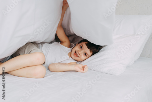 Little boy hiding under the covers in the bed, sunny bedroom. Child woke up cheerful morning © sushytska