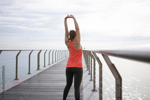 Fototapeta Naklejka Na Ścianę i Meble -  
Young athletic woman doing stretching exercises for arms while standing on the bridge