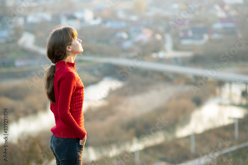 Young woman in red jacket standing outdoors enjoying evening view. Relaxing, freedom and wellness concept.
