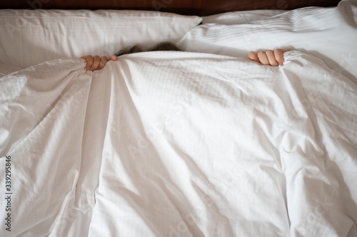 
Woman hiding under blanket in bed