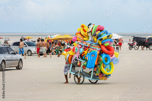 Vendedor de brinquedos infláveis coloridos andando na areia da praia com seu carrinho entre os carros. photo