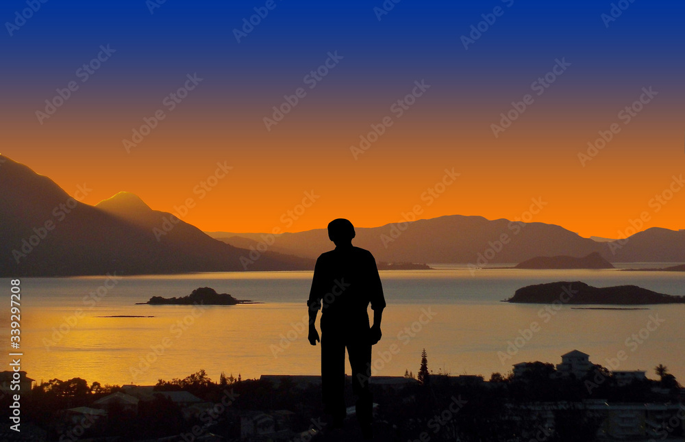 Evening, sunset. A man stands on a hill and looks out at the sea