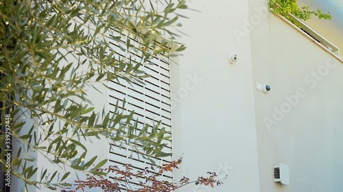 Outdoor smart home professional security cameras system. Electric rolling shutter opening on a window. Wide shot with a low angle.