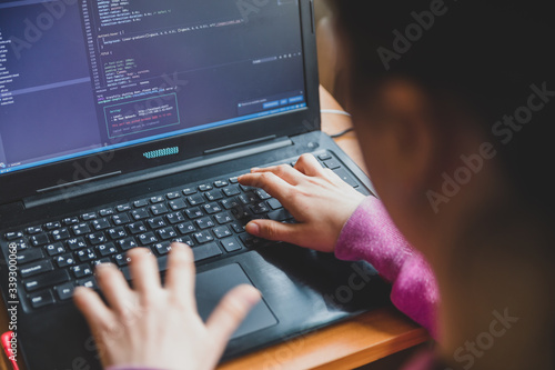 Young caucasian girl in pink sweater at computer while studying online programming at home near the window