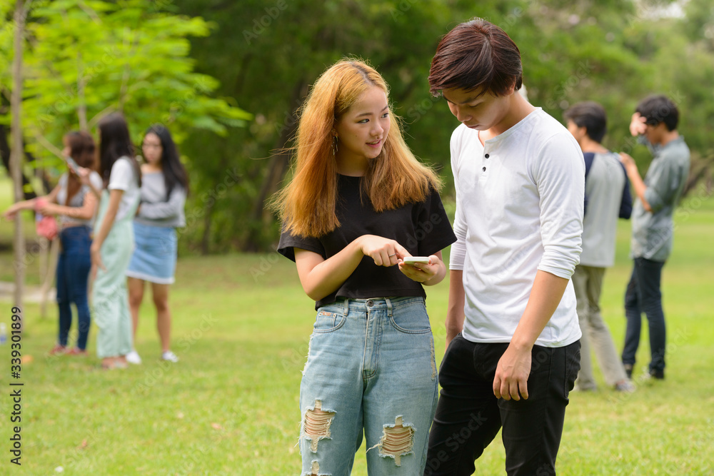 Young Asian couple using phone together with friends at the park Young Asian couple using phone together with friends at the park