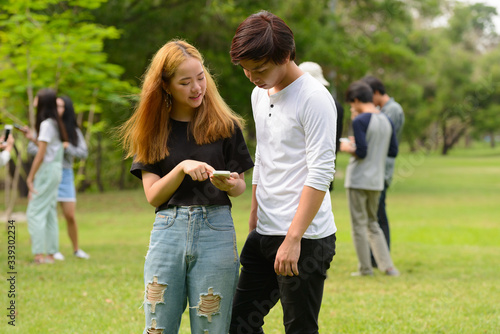 Young Asian couple using phone together with friends at the park