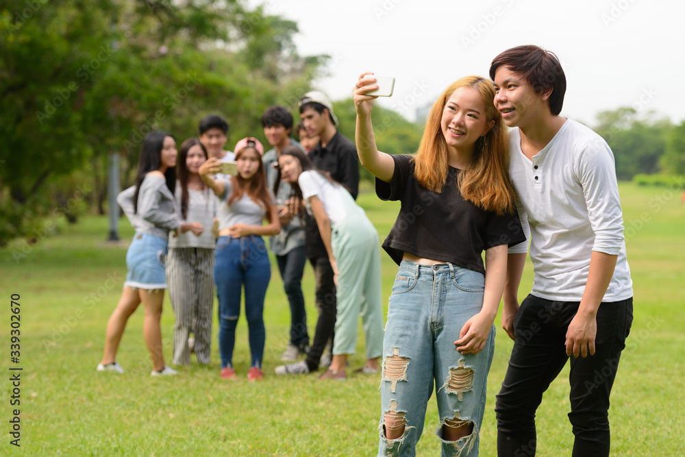 Happy young Asian couple taking selfie together with friends at the park Happy young Asian couple taking selfie together with friends at the park