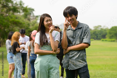 Happy young Asian couple thinking together with friends at the park