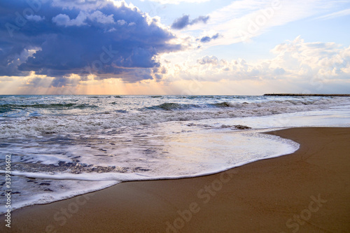 tropical sandy beach with waves and foam at sunset with a big cloud in the sky