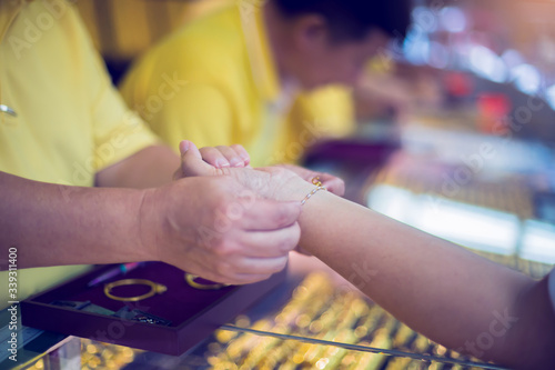 The hands of women customers and salespeople trying to wear bracelets of various types of gold jewelry. Yaowarat gold shop, Thailand