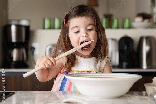 Cute toddler girl tasting food in kitchen photo