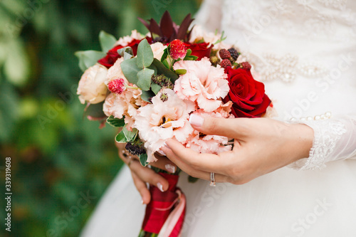 Beautiful red wedding flowers bouquet in hands of the bride.