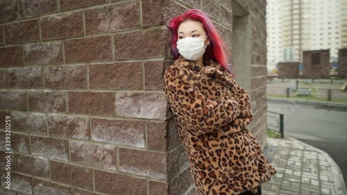 Concept: urban healthcare during pollution pandemic. Beautiful young asian girl with colored hair in medical mask wearing grunge fashion clothing standing street