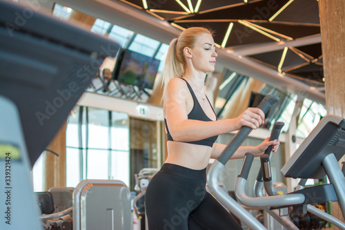 Young fitness woman working out on an elliptical trainer in gym