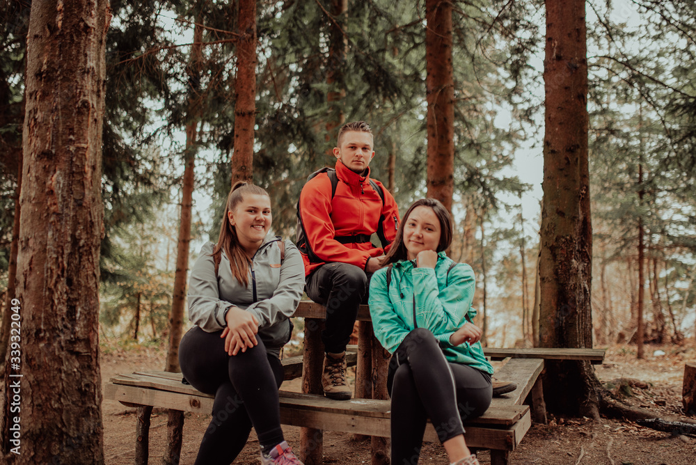 Three young adult friends taking a break sitting on wood desk in forest 