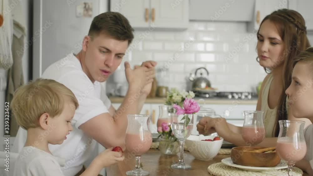 Close up of happy family sitting around kitchen table in the morning eating breakfast together and having fun Close up of happy family sitting around kitchen table in the morning eating breakfast together and having fun