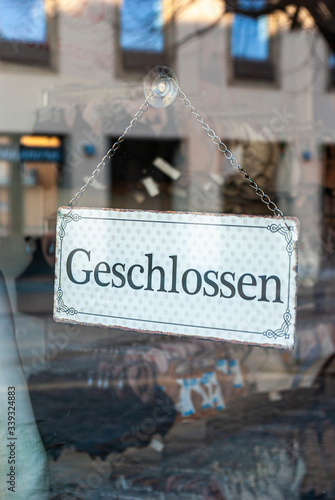 Schaufenster von Ladengeschäft mit Schild „Geschlossen“, in Deutsch, mit Auslagen und die Spiegelung der Umgebung in Unschärfe zur Zeit der Corona Covid-19 Pandemie im März 2020