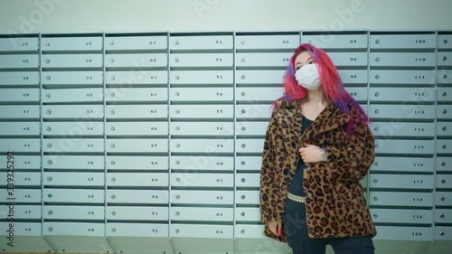 Concept: urban healthcare during pollution pandemic. Beautiful young asian girl colored hair medical mask grunge fashion clothing standing near mailboxes in apartment house
