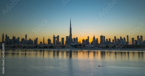 Sunrise in Dubai hyperlapse or timelapse view from boat or sea. The Sun rises over UAE skyscrapers at morning. Camera moves along beach, coast, shore.