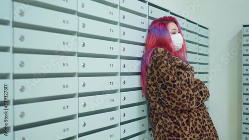 Concept: urban healthcare during pollution pandemic. Beautiful young asian girl colored hair medical mask grunge fashion clothing standing near mailboxes in apartment house