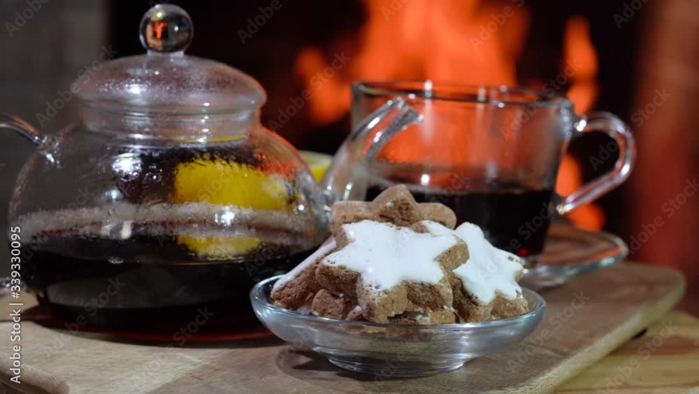 The table with Glass teapot , cup of hot tea and lemon is rotating before cozy fireplace, in country house, vacation. The table with Glass teapot , cup of hot tea and lemon is rotating before cozy fireplace, in country house, vacation.