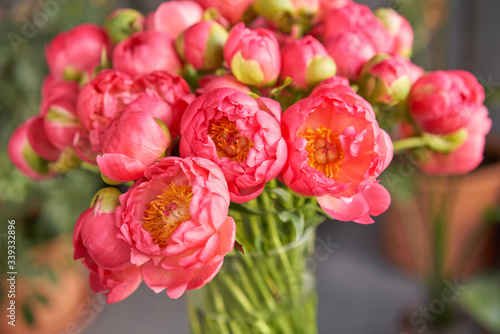 Fototapeta Naklejka Na Ścianę i Meble -  Coral peonies in a glass vase on wooden table. Beautiful peony flower for catalog or online store. Floral shop concept . Beautiful fresh cut bouquet. Flowers delivery.