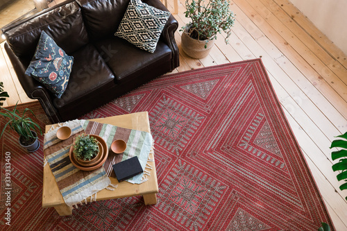 clay plates and a book on a wooden table with ethnic woven rugs. A vase of flowers and a leather sofa clay plates and a book on a wooden table with ethnic woven rugs. red wool carpet