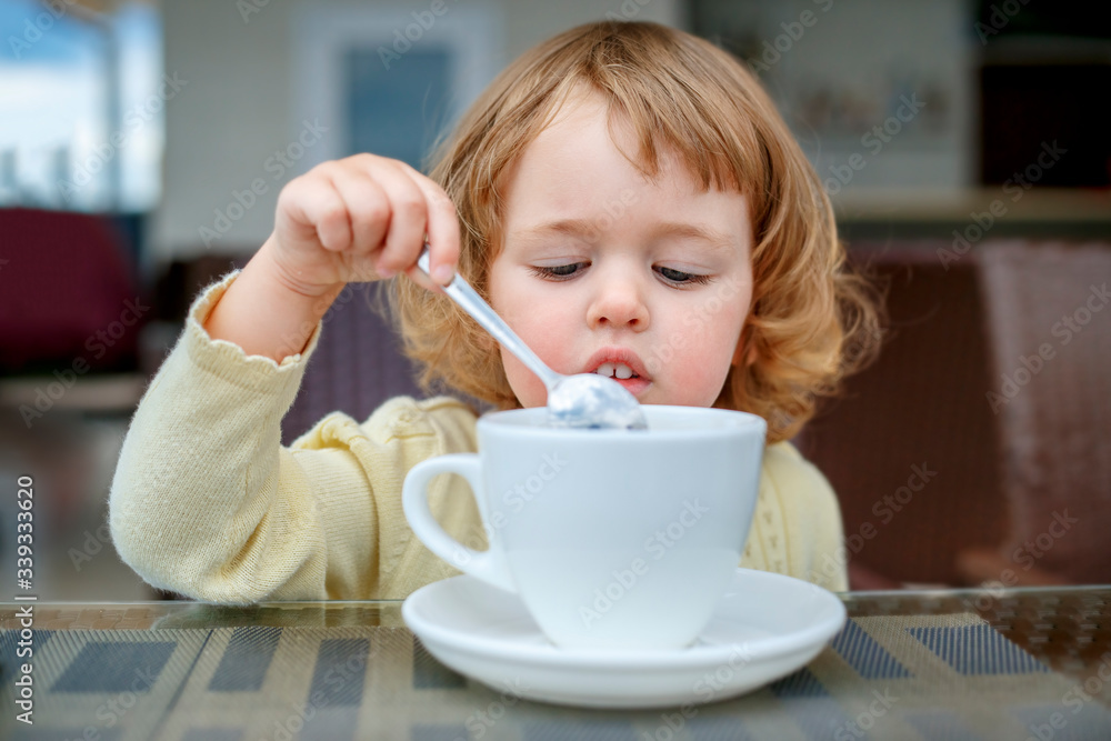 Adorable 2 years old little girl drinking mug coffee tea hot drink in outdoor cafe. Healthy eating for kids. Travel with young children. Adorable 2 years old little girl drinking mug coffee tea hot drink in outdoor cafe. Healthy eating for kids. Travel with young children.